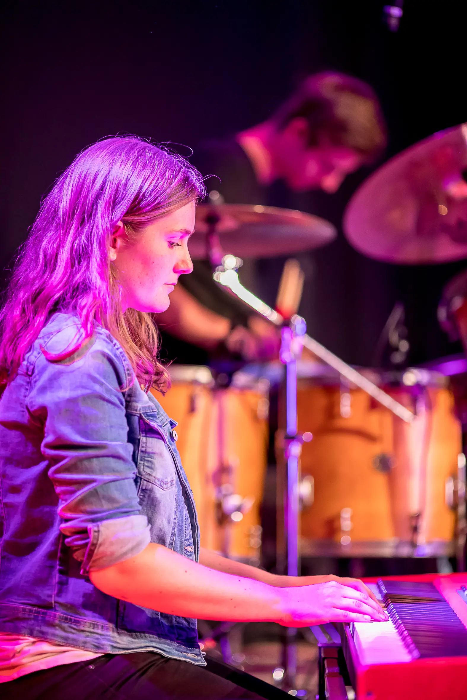 Toetseniste achter het keyboard, drummer onscherp op de achtergrond